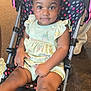 Maliya is registered to the contest to win money with this photo: toddler, child, stroller, polka_dot, hair_buns, indoor, clothing, green_dress, sitting, curious, baby, person, cute, infant, legs, face, seat, footwear, hand, background