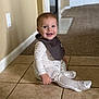 baby, child, sitting, smiling, pajamas, bib, floor, tile_floor, carpet, indoor, home, door, wall, happy, portrait, person, cute, young, infant, clothing