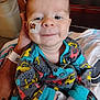 baby, bed, blanket, child, clothing, cute, face, feeding_tube, hand, healthcare, hospital, indoors, infant, medical_tape, onesie, person, sleeves, smile, tattoo, vehicle_pattern