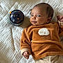 baby, infant, quilt, brown_sweater, sheep_patch, toy, musical_toy, stars, bed, blanket, child, cute, soft_texture, smile, face, hand, relaxing, indoors, cozy, portrait