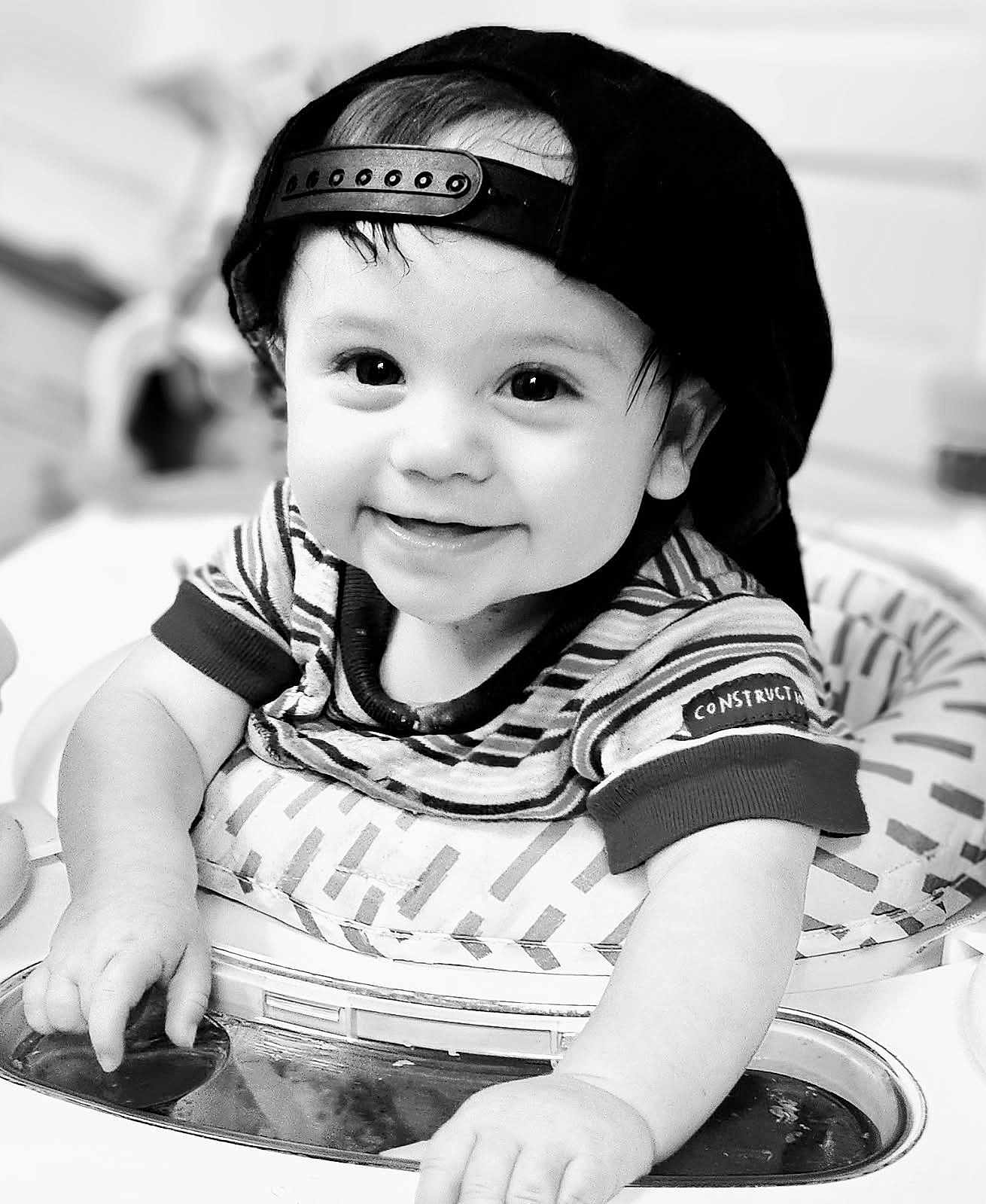 Rhyland joined the competition — help win amazing prizes! baby, child, smiling, face, cap, hat, striped_shirt, high_chair, hand, cute, infant, portrait, black_and_white, happy, young, person, indoors, expression, playful, toddler