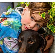 Wanda participe au concours pour gagner de l'argent avec cette photo : child, dog, hug, outdoor, greenery, leaves, wall, colorful_clothing, portrait, friendship, animal, pet, closeup, boy, affection, nature, casual, happy, cute, companion