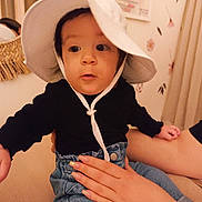Théa participe au concours pour gagner de l'argent avec cette photo : baby, black_clothing, child, couch, cozy, curious, denim_pants, face, furniture, glitter_nails, hand, hat, indoor, nails, person, portrait, sitting, soft_lighting, white_hat, young_child