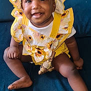 Ily participe au concours pour gagner de l'argent avec cette photo : baby, smiling, child, yellow_clothing, bonnet, sunflower_pattern, crocheted_toy, blue_couch, sitting, happy, cute, infant, indoors, portrait, face, person, young_child, playful, cheerful, clothing