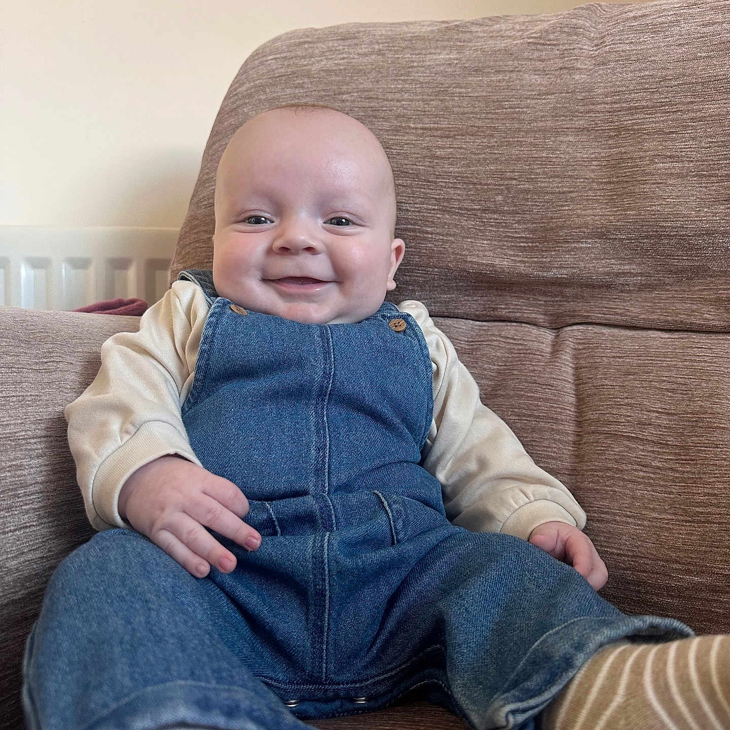Bohdi is registered to the contest to win money with this photo: baby, casual, child, clothing, couch, cozy, cute, denim_overalls, face, furniture, happy, head, indoor, infant, person, portrait, relaxing, sitting, smile, sock