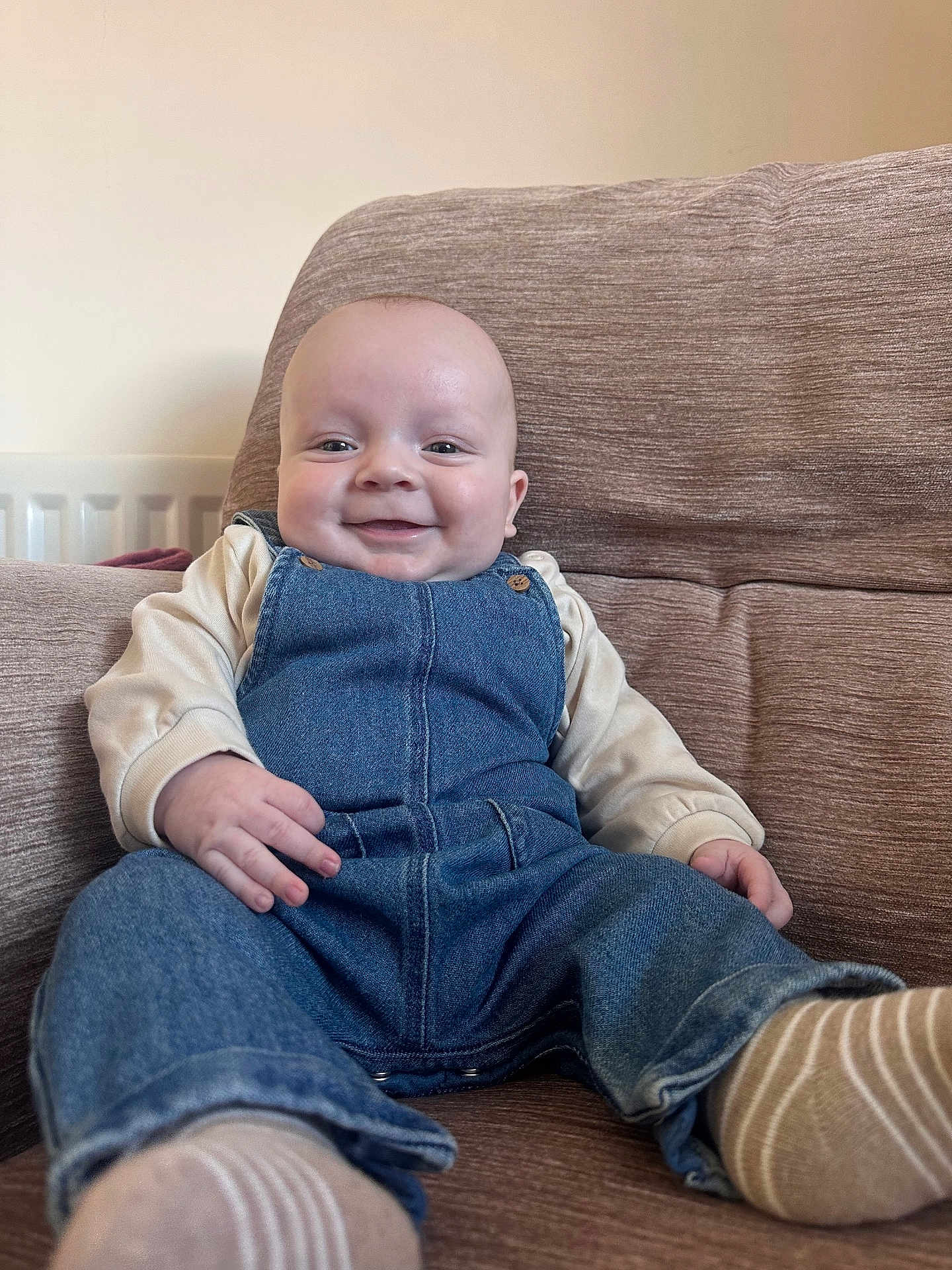 Bohdi is registered to the contest to win money with this photo: baby, denim_overalls, smile, couch, infant, happy, child, clothing, sitting, indoor, portrait, cute, person, cozy, relaxing, furniture, head, face, sock, casual