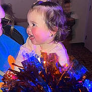 Brae joined the competition — help win amazing prizes! toddler, child, person, face, hair, pony_tail, smile, tongue, cheeks, pom_poms, colorful, blue_light, orange_light, indoor, blurred_background, happy, joyful, holding, clothing, playful