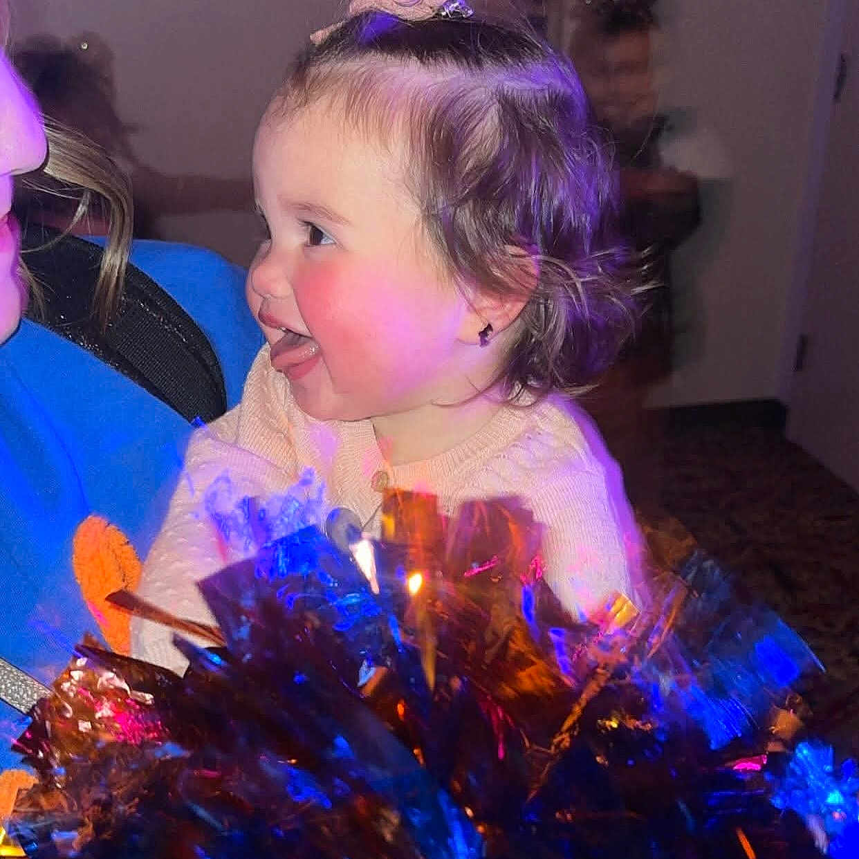 Brae joined the competition — help win amazing prizes! blue_light, blurred_background, cheeks, child, clothing, colorful, face, hair, happy, holding, indoor, joyful, orange_light, person, playful, pom_poms, pony_tail, smile, toddler, tongue