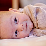 Colton is registered to the contest to win money with this photo: baby, infant, face, eyes, smile, sweater, lying_down, closeup, portrait, skin, head, cute, warm_clothing, indoors, soft_light, expression, newborn, child, peaceful, resting