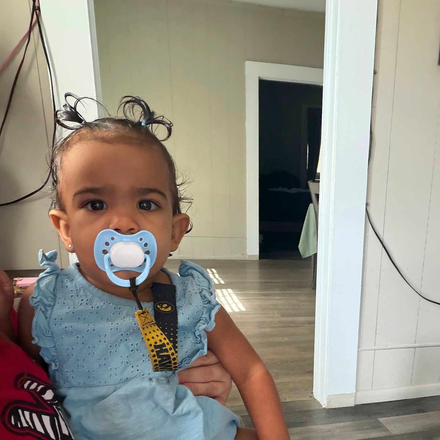 Ada joined the competition — help win amazing prizes! toddler, baby, pacifier, blue_dress, child, indoor, person, hair_ties, curly_hair, holding, adult_hand, flooring, doorway, wall, earrings, clothing, expression, light, room, home_interior