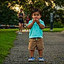 Malachi is registered to the contest to win money with this photo: toddler, child, boy, park, pathway, grass, trees, shorts, polo_shirt, blue_shoes, walking, people, outdoor, nature, sunset, casual_clothing, person, portrait, summer, daytime