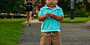 Malachi is registered to the contest to win money with this photo: toddler, child, park, path, grass, greenery, person, walking, shorts, polo_shirt, blue_shoes, cartoon_shoes, outdoor, daylight, summer, nature, blurred_background, casual_clothing, standing, portrait