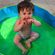 Eliott a rejoint le concours — aidez-le/la à gagner de superbes lots ! toddler, child, pool, water, sitting, playful, wet_hair, summer, outdoor, sunlight, green, blue, skin, barefoot, diaper, happy, cute, baby, fun, splash