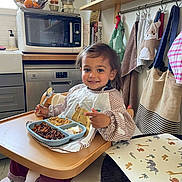 Sacha a rejoint le concours — aidez-le/la à gagner de superbes lots ! bags, bib, child, dishwasher, food, happy, high_chair, home_interior, indoor, kitchen, meal, microwave, pajamas, plate, smile, spoon, table, toddler, towels, window