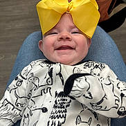 Kaylee is registered to the contest to win money with this photo: baby, smiling, yellow_bow, onesie, dog_pattern, infant, happy, clothing, person, portrait, indoor, lap, cute, child, headwear, fabric, young_child, human, closeup, face