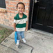 Giovanni joined the competition — help win amazing prizes! child, boy, smiling, standing, brick_wall, black_door, toy, blue_toy, casual_clothing, green_and_white_shirt, jeans, white_shoes, concrete_sidewalk, outdoor, happy, portrait, person, young_child, short_hair, daylight