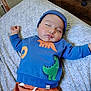 baby, sleeping, child, blue_sweater, dinosaur_patch, orange_pants, bed, blanket, indoor, peaceful, cute, infant, headwear, resting, cozy, soft_lighting, face, person, toddler, clothing