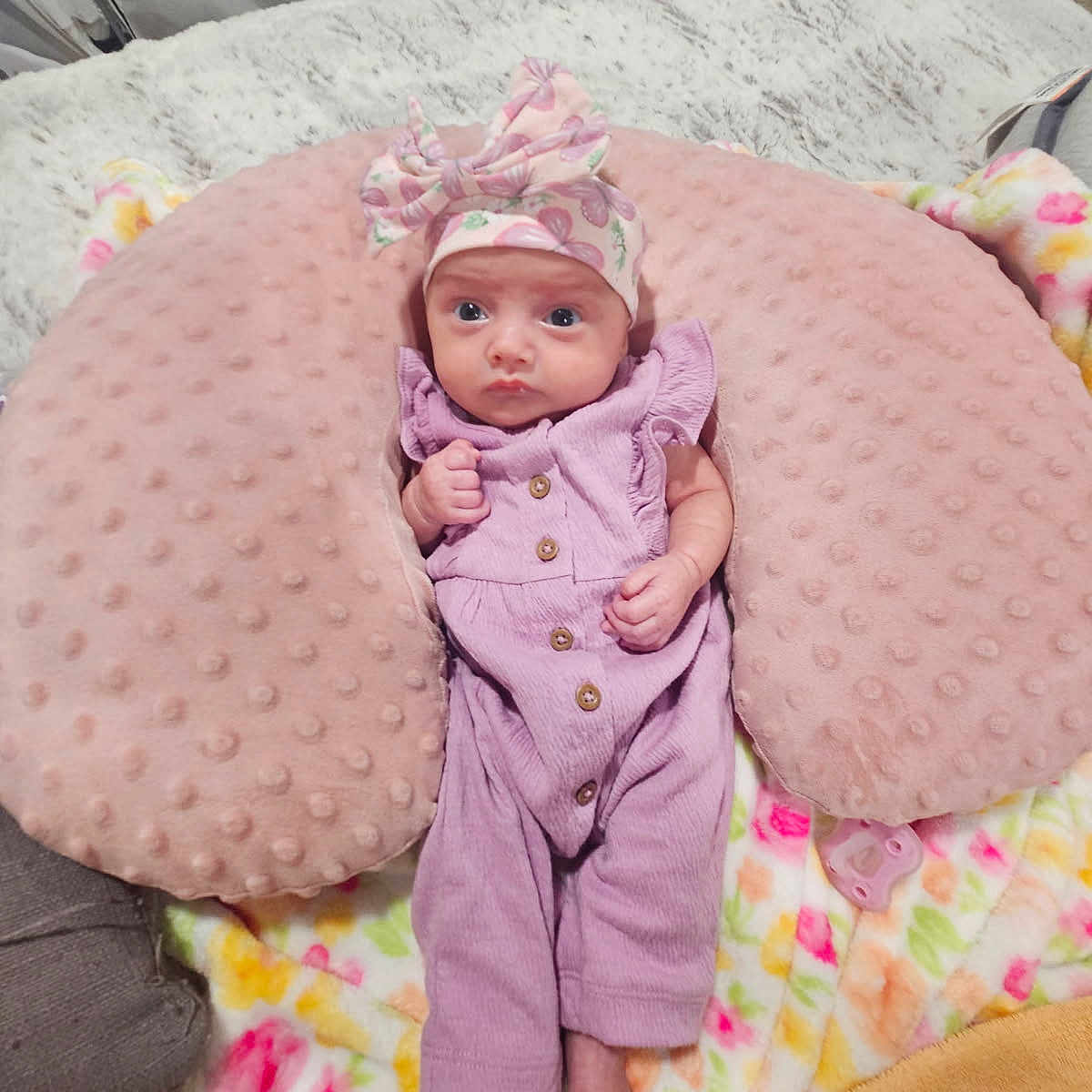 Susanna is registered to the contest to win money with this photo: baby, bed, blanket, bow, child, cozy, cute, feet, fist, floral_pattern, headband, indoor, infant, newborn, person, pink_pillow, purple_outfit, resting, sleeping_area, soft_texture