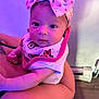Lyrica is registered to the contest to win money with this photo: baby, child, headband, bow, bib, person, infant, cute, purple_lighting, indoor, holding, skin, face, eyes, expression, clothing, floor, wall, arm, newborn