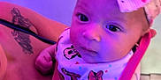 Lyrica is registered to the contest to win money with this photo: baby, infant, headband, bow, bib, tattoo, arm, person, child, purple_light, indoor, cute, young, holding, face, eyes, clothing, skin, portrait, expression