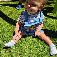 Asher is registered to the contest to win money with this photo: child, toddler, grass, outdoor, sunlight, toy_story, overalls, shirt, socks, baby, person, cute, shadow, nature, playing, summer, daylight, expression, sitting, footwear
