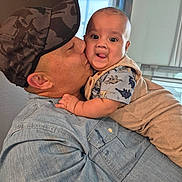 Ivan joined the competition — help win amazing prizes! adult, affection, baby, camo_cap, casual_clothing, close_up, denim_shirt, dinosaur_print, expression, face, family, happy, holding, indoor, kiss, love, overalls, person, television, tongue_out