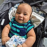 baby, child, stroller, blanket, striped_shirt, smile, face, arm, clothing, fabric, pattern, comfort, cute, infant, portrait, outdoor, hand, seat, head, expression