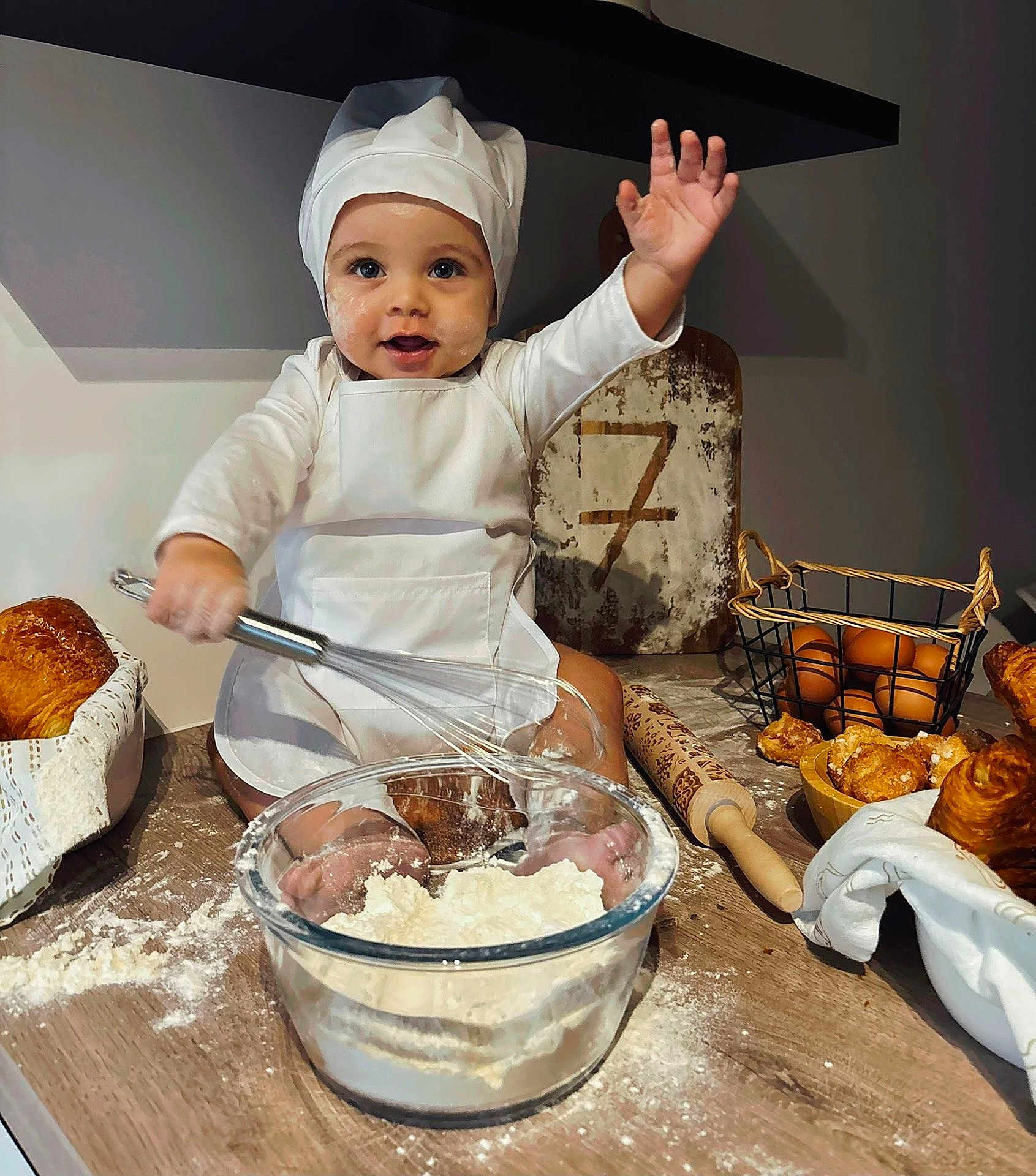 Hayden a rejoint le concours — aidez-le/la à gagner de superbes lots ! baby, child, chef_hat, whisk, flour, baking, kitchen, croissants, eggs, rolling_pin, basket, apron, smiling, messy, countertop, food, cute, cooking, portrait, happy