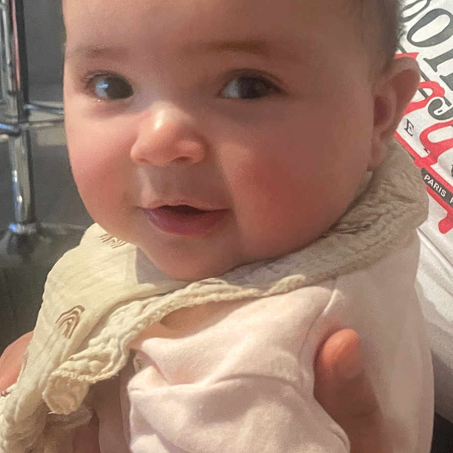 Eline participe au concours pour gagner de l'argent avec cette photo : baby, bib, child, closeup, clothing, curly_hair, cute, expression, face, hand, holding, indoor, infant, person, portrait, skin, smile, soft_light, warm, young_child