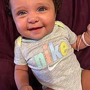 Maselynn is registered to the contest to win money with this photo: apparel, baby, bracelet, cheerful, child, closeup, clothing, curly_hair, cute, face, hand, happy, indoor, infant, lying_down, onesie, person, skin, smile, text_on_clothing