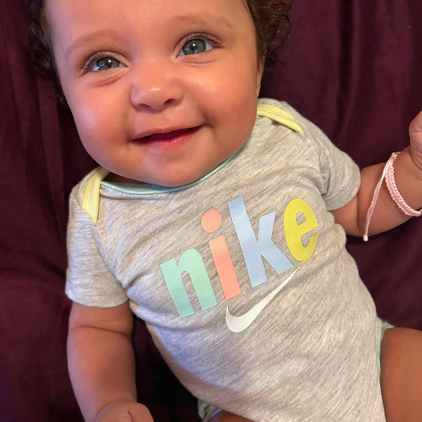Maselynn is registered to the contest to win money with this photo: apparel, baby, bracelet, cheerful, child, closeup, clothing, curly_hair, cute, face, hand, happy, indoor, infant, lying_down, onesie, person, skin, smile, text_on_clothing
