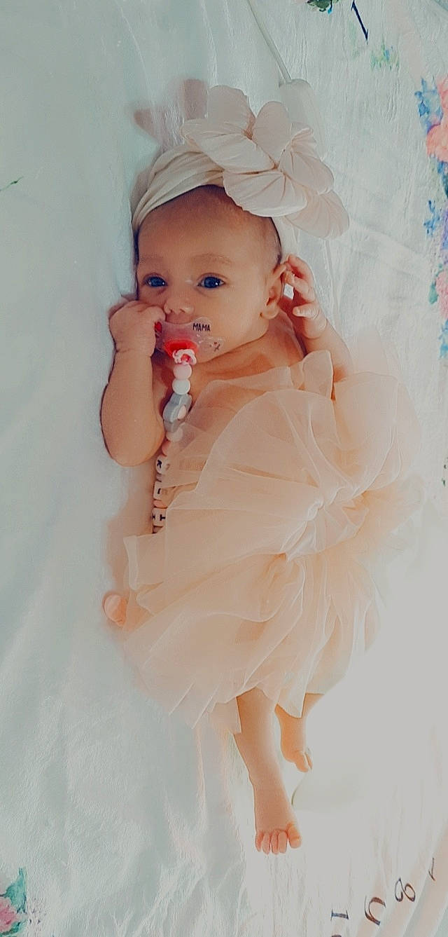 Keïssy participe au concours pour gagner de l'argent avec cette photo : baby, baby_toddler_clothing, cap, dress, embellishment, eye, face, gesture, happy, headgear, headpiece, iris, jewellery, lip, nail, person, pink, skin, sleeve, thumb