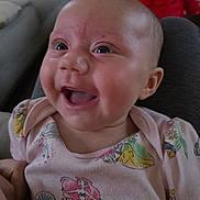 Mia is registered to the contest to win money with this photo: baby, smiling, indoor, child, face, clothing, pink_shirt, mermaid_pattern, happy, cute, person, infant, portrait, sitting, plush_toy, background, couch, cozy, head, eyes