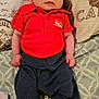 Lucas is registered to the contest to win money with this photo: baby, infant, red_shirt, dark_pants, white_socks, lying_down, bedspread, patterned_bedspread, face, person, child, cute, small_hands, newborn, portrait, indoors, fabric, textile, clothing, resting