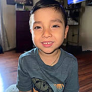 Kyrie is registered to the contest to win money with this photo: child, boy, smiling, indoor, tshirt, dinosaur, hair, face, portrait, living_room, furniture, wooden_floor, television, painting, necklace, casual_clothing, happy, cute, closeup, young