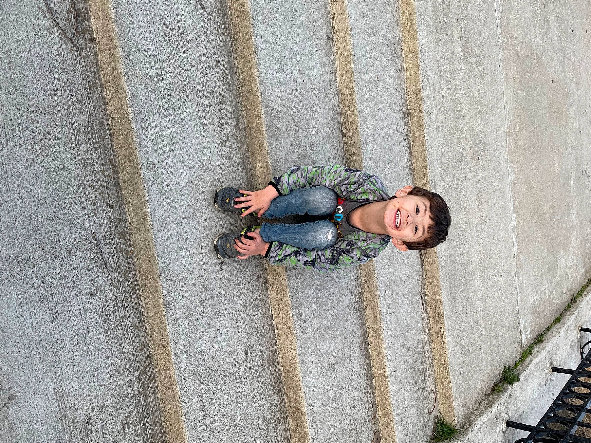 Jaxon is registered to the contest to win money with this photo: asphalt, cement, concrete, denim, eyewear, grey, human_leg, joy, leisure, pattern, pedestrian, person, recreation, road, road_surface, shadow, sidewalk, sitting, street, street_fashion