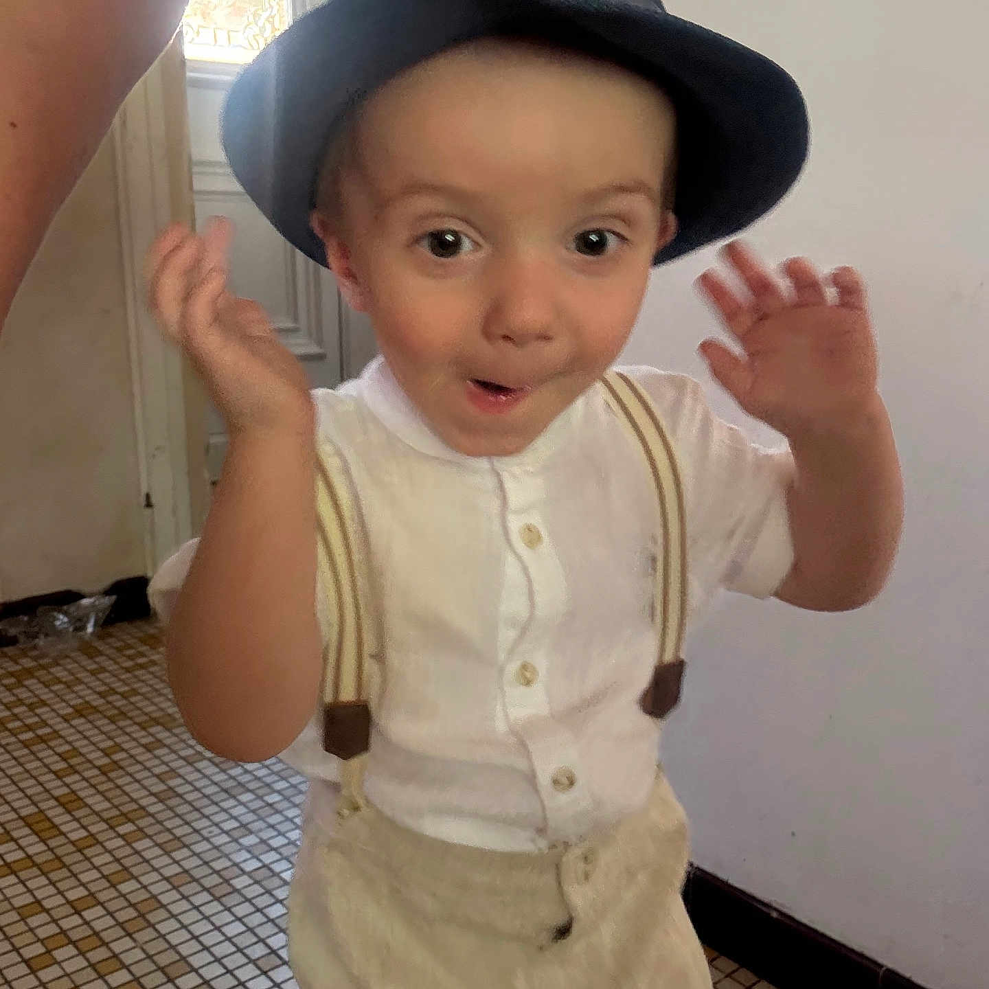 Thymaël participe au concours pour gagner de l'argent avec cette photo : boy, casual_clothing, child, cream_pants, cute, door, face, hands_up, hat, home, indoor, person, portrait, smiling, standing, surprised_expression, suspenders, tiled_floor, white_shirt, young_child