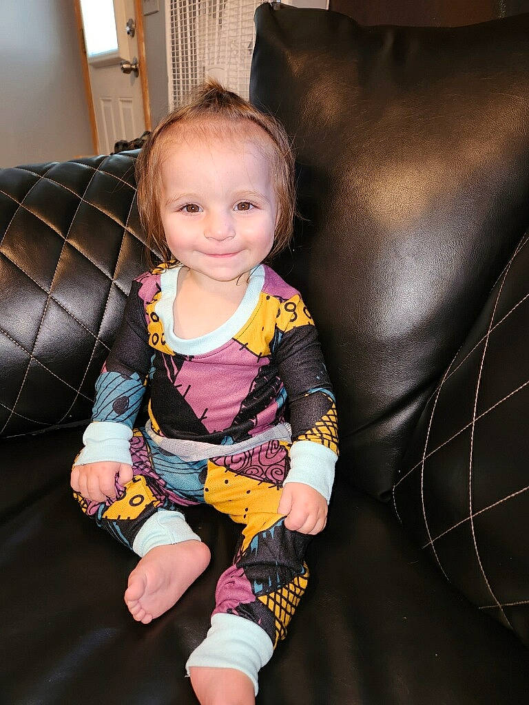 Oaklyn is registered to the contest to win money with this photo: baby, baby_toddler_clothing, chair, cheek, child, comfort, couch, fun, furniture, hairstyle, human_leg, joy, knee, lap, pattern, person, purple, sitting, sleeve, smile