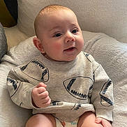 Felix is registered to the contest to win money with this photo: baby, infant, child, sitting, sweatshirt, football_pattern, diaper, soft_surface, plush, cute, smiling, indoor, portrait, young_child, hand, face, skin, head, comfortable, clothing