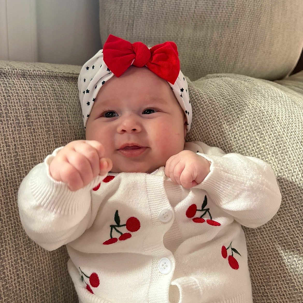 Eysmë a rejoint le concours — aidez-le/la à gagner de superbes lots ! baby, bow, cherry, child, couch, cozy, cute, face, furniture, hands, headband, indoor, infant, knitwear, portrait, red, smiling, soft, sweater, white