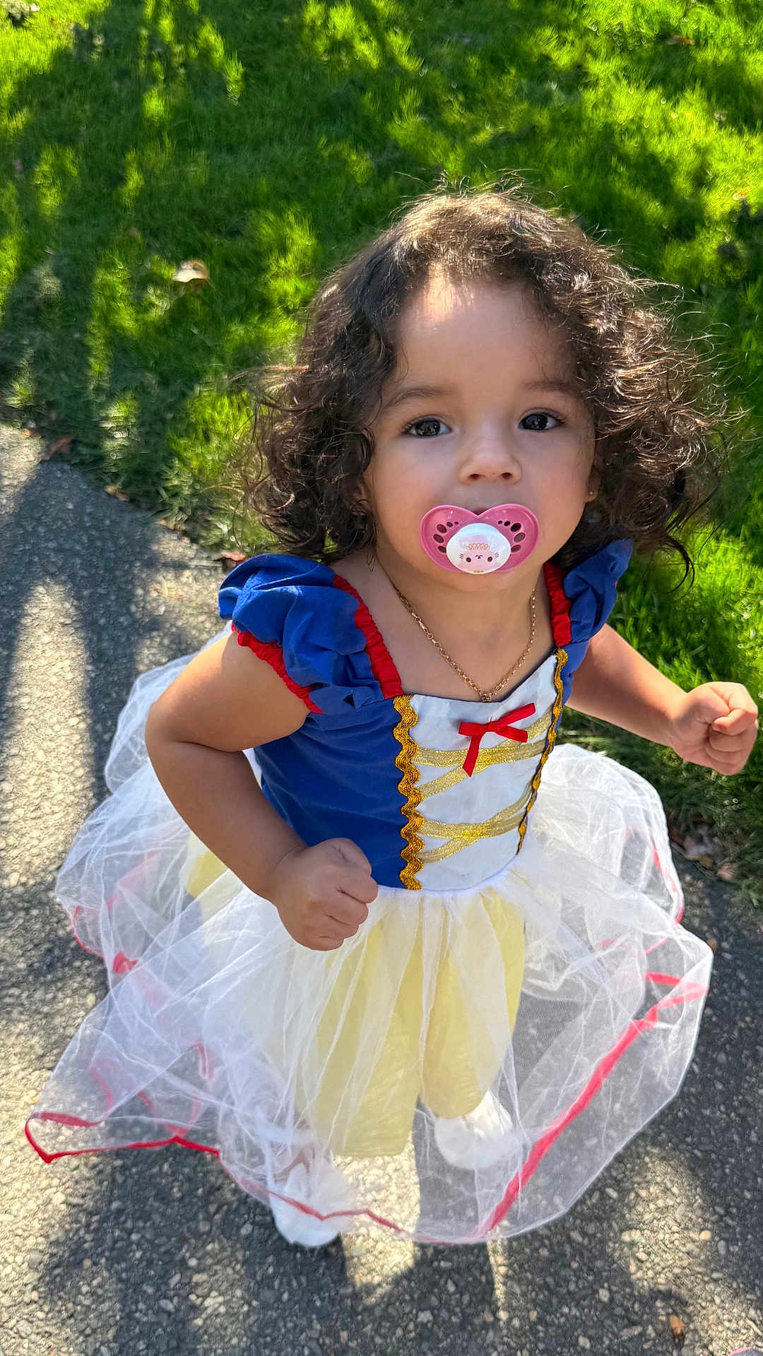 Maria Helena joined the competition — help win amazing prizes! toddler, child, pacifier, curly_hair, princess_dress, costume, outdoor, daylight, grass, sidewalk, blue_dress, white_tulle, red_trim, gold_detail, necklace, portrait, cute, young_child, person, smile
