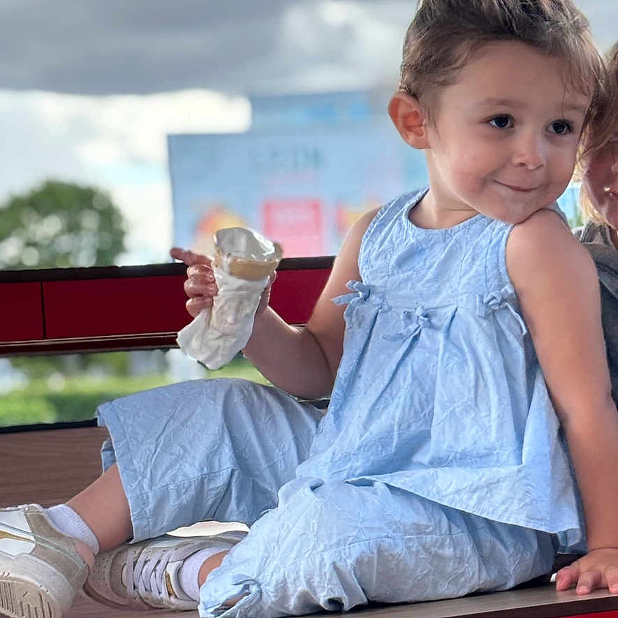 Jennah a rejoint le concours — aidez-le/la à gagner de superbes lots ! blue_clothing, casual, child, cloudy_sky, cute, daylight, fun, happy, ice_cream, outdoor, person, playful, portrait, sitting, smile, snack, summer, table, white_shoes, young_child