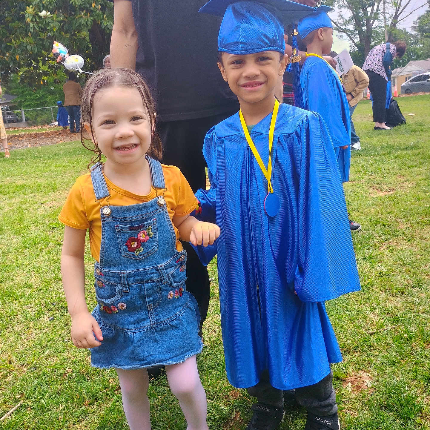 Luna Owens is registered to the contest to win money with this photo: adult, background, cap_and_gown, celebration, child, children, daylight, denim_overalls, event, glasses, graduation, grass, happy, medal, outdoor, person, shoes, smiling, tree, yellow_shirt