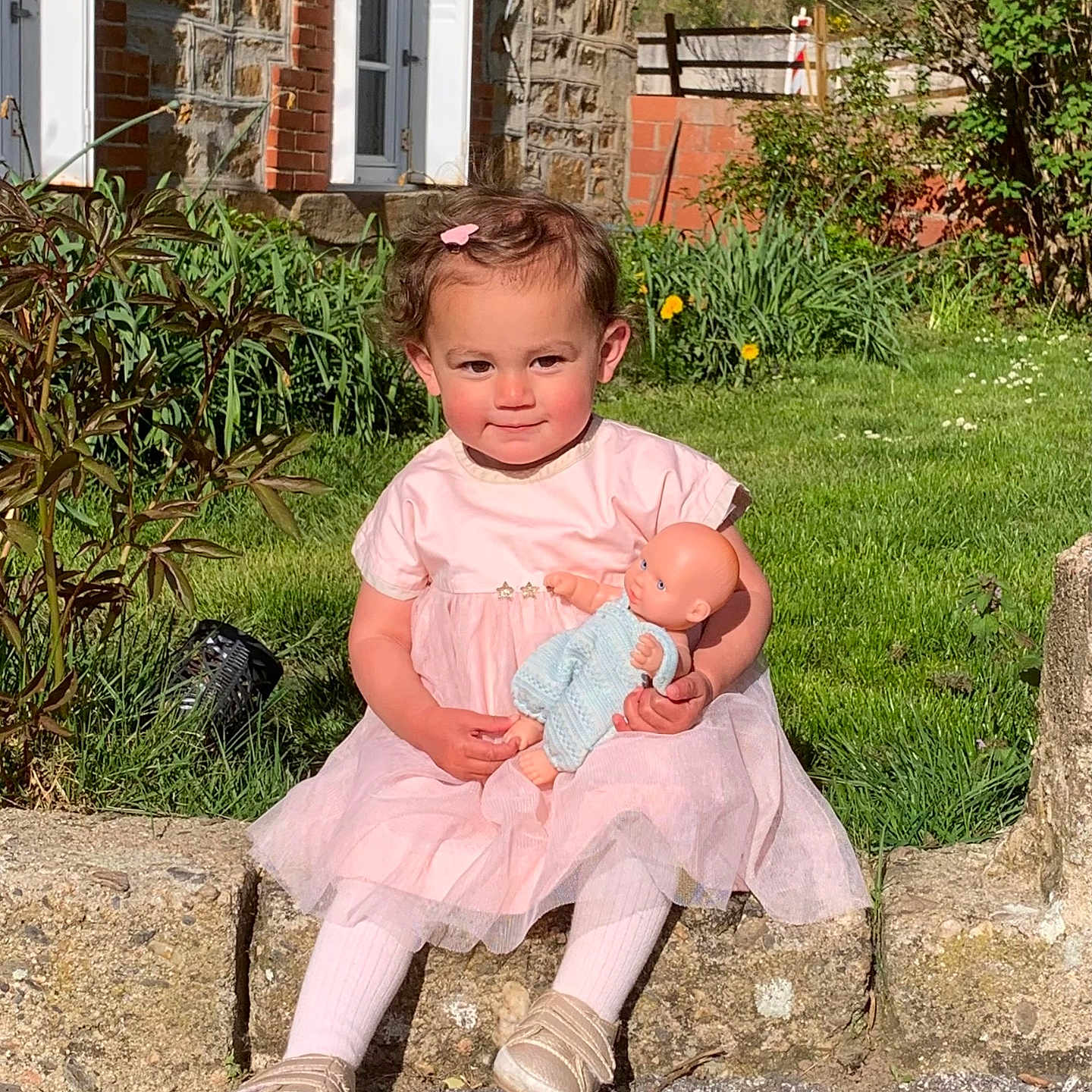 Lina a rejoint le concours — aidez-le/la à gagner de superbes lots ! toddler, child, pink_dress, doll, outdoor, grass, stone_wall, brick_house, greenery, sunlight, smiling, cute, toy, baby, person, garden, shoes, hair_clip, nature, portrait
