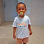 toddler, child, pacifier, white_tshirt, shorts, sandals, indoor, floor, door, wall, smile, standing, person, young_child, clothing, footwear, head, face, happy, casual