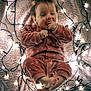 baby, infant, onesie, pink_clothing, fairy_lights, blanket, cozy, cute, child, indoors, portrait, smiling, feet, hands, face, soft_lighting, warm_tones, sleepwear, resting, toddler