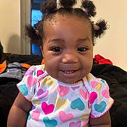 Tycelynn is registered to the contest to win money with this photo: toddler, child, smile, hair_buns, colorful_clothing, heart_pattern, indoor, person, cute, happy, baby, portrait, short_sleeves, skin, face, young_child, seated, casual, cozy, background