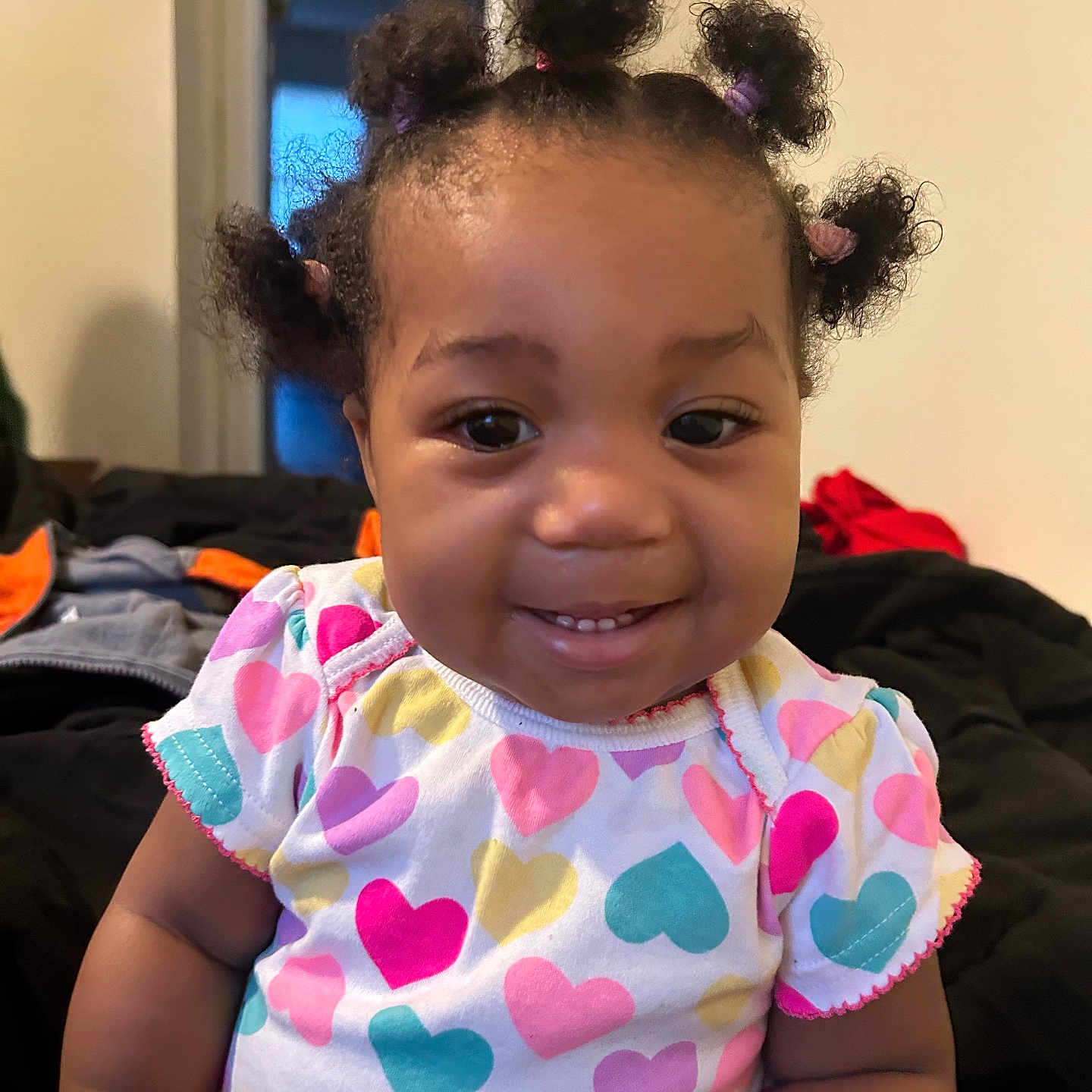 Tycelynn is registered to the contest to win money with this photo: toddler, child, smile, hair_buns, colorful_clothing, heart_pattern, indoor, person, cute, happy, baby, portrait, short_sleeves, skin, face, young_child, seated, casual, cozy, background