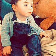 Wyley participe au concours pour gagner de l'argent avec cette photo : toddler, child, denim_overalls, cardigan, blanket, plush_toy, sofa, indoor, casual_clothing, socks, curly_hair, cute, seated, soft_toys, home, floor_tiles, wooden_stool, pillow, relaxed, portrait