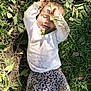 toddler, child, grass, leaves, dirt, outdoor, playful, smiling, white_shirt, floral_pants, nature, happy, messy, sunlight, person, young_child, casual_clothing, relaxing, lying_down, daytime